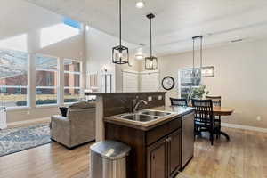 Kitchen featuring decorative light fixtures, sink, stainless steel dishwasher, dark brown cabinets, and a center island with sink