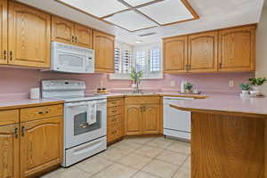 Kitchen featuring sink, white appliances, light tile patterned floors, and a textured ceiling