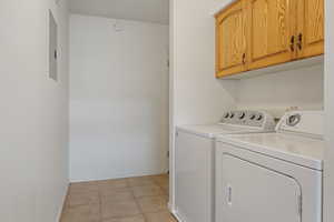 Clothes washing area with light tile patterned flooring, cabinets, and washer and clothes dryer