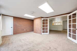 Carpeted empty room featuring french doors and brick wall