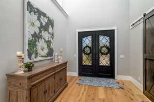 Foyer entrance with french doors, a towering ceiling, a barn door, and light wood-type flooring