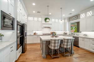 Kitchen with a breakfast bar area, stainless steel appliances, a center island, white cabinets, and decorative light fixtures