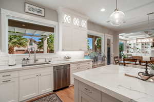 Kitchen featuring sink, hanging light fixtures, dishwasher, white cabinets, and backsplash