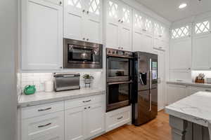 Kitchen with stainless steel microwave, refrigerator with ice dispenser, double wall oven, and white cabinets