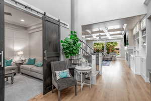 Living room featuring beamed ceiling, ornamental molding, coffered ceiling, light hardwood / wood-style floors, and a barn door