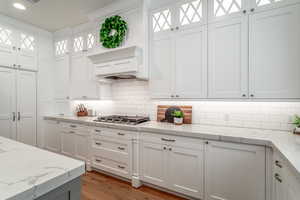 Kitchen featuring stainless steel gas stovetop, white cabinets, and light stone counters