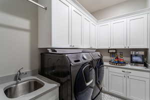 Laundry room featuring sink, washer and clothes dryer, and cabinets