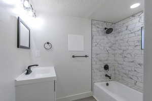 Bathroom with vanity, a textured ceiling, and tiled shower / bath