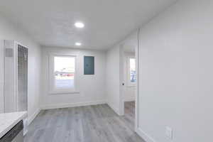 Unfurnished room with electric panel, light hardwood / wood-style floors, and a textured ceiling