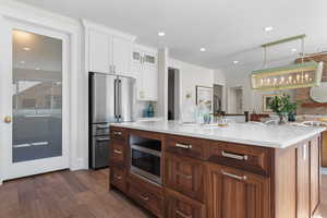 Kitchen featuring decorative light fixtures, appliances with stainless steel finishes, dark hardwood / wood-style flooring, a kitchen island with sink, and white cabinets