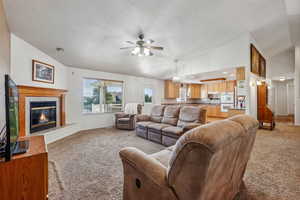 Living room featuring high vaulted ceiling, sink, a tiled fireplace, ceiling fan, and light carpet