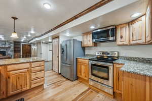 Kitchen with a stone fireplace, hanging light fixtures, stainless steel appliances, light stone countertops, and light hardwood / wood-style floors