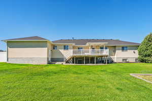 Rear view of house with a wooden deck and a lawn