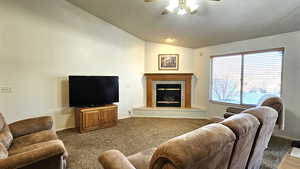 Living room with dark carpet, ceiling fan, vaulted ceiling, and a tile fireplace