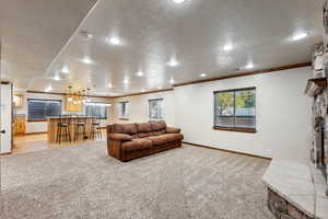 Carpeted living room featuring ornamental molding, a stone fireplace, bar area, and a textured ceiling