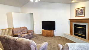 Carpeted living room featuring a tile fireplace, lofted ceiling, and ceiling fan