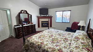 Bedroom with lofted ceiling, a fireplace, dark carpet, and a textured ceiling