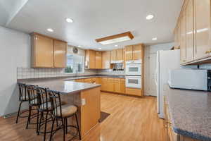 Kitchen with a kitchen bar, decorative backsplash, white appliances, light brown cabinets, and light wood-type flooring