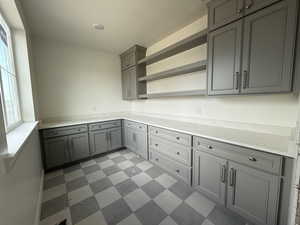 Kitchen featuring light stone countertops, gray cabinetry, open shelves, and light floors