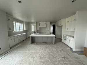 Kitchen featuring a center island, baseboards, white cabinetry, and custom exhaust hood