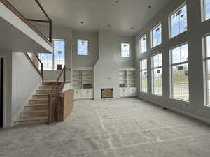 Unfurnished living room with baseboards, a high ceiling, stairs, and built in shelves
