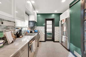 Kitchen featuring tile walls, sink, stainless steel appliances, and white cabinets