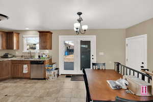 Kitchen with decorative light fixtures, sink, a chandelier, stainless steel dishwasher, and light stone counters