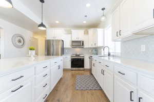 Kitchen featuring appliances with stainless steel finishes, white cabinetry, sink, hanging light fixtures, and light hardwood / wood-style floors