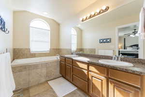 Bathroom featuring lofted ceiling, tiled bath, tile patterned flooring, vanity, and ceiling fan