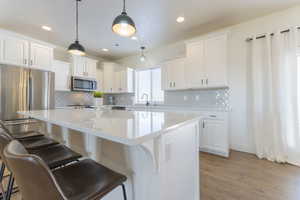 Kitchen featuring a breakfast bar, white cabinetry, decorative light fixtures, a center island, and appliances with stainless steel finishes