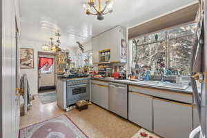 Kitchen featuring sink, white cabinetry, stainless steel appliances, a notable chandelier, and decorative light fixtures