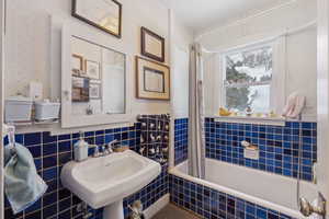 Bathroom featuring shower / bathtub combination with curtain, sink, and tile walls