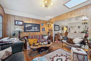 Living room featuring wood-type flooring, a notable chandelier, wooden walls, and a skylight