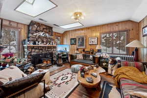 Living room featuring wood-type flooring, vaulted ceiling with skylight, and wood walls