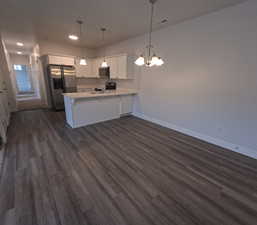 Kitchen with appliances with stainless steel finishes, white cabinets, dark hardwood / wood-style flooring, decorative light fixtures, and kitchen peninsula