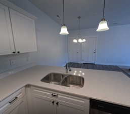 Kitchen with dishwasher, sink, white cabinets, and decorative light fixtures