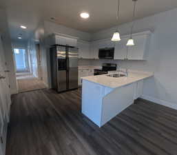 Kitchen with white cabinetry, sink, hanging light fixtures, kitchen peninsula, and stainless steel appliances