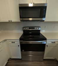 Kitchen with white cabinetry, stainless steel appliances, dark hardwood / wood-style floors, and light stone countertops