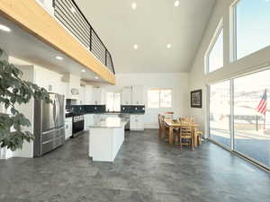 Kitchen featuring appliances with stainless steel finishes, high vaulted ceiling, white cabinets, backsplash, and a center island