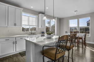 Kitchen with white cabinetry, sink, decorative light fixtures, and a kitchen island