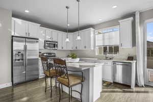 Kitchen featuring a kitchen island, pendant lighting, white cabinetry, sink, and stainless steel appliances