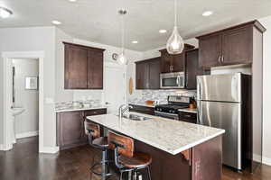 Kitchen featuring dark brown cabinetry, sink, decorative light fixtures, a center island with sink, and stainless steel appliances