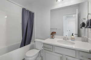 Full bathroom with vanity, shower / bathtub combination with curtain, and toilet