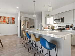 Kitchen with a kitchen island with sink, decorative light fixtures, gray cabinets, and appliances with stainless steel finishes