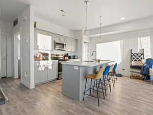 Kitchen featuring sink, light hardwood / wood-style flooring, gray cabinetry, hanging light fixtures, and stainless steel appliances