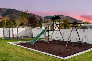 Playground at dusk with a mountain view, a yard, and a trampoline