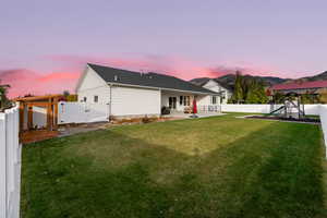 Back house at dusk featuring a lawn, a patio, and a playground