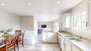 Kitchen featuring sink, stainless steel dishwasher, kitchen peninsula, light hardwood / wood-style floors, and white cabinets