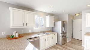 Kitchen with appliances with stainless steel finishes, sink, white cabinets, and light hardwood / wood-style flooring