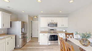 Kitchen with white cabinetry, appliances with stainless steel finishes, and light wood-type flooring